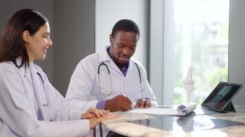 i en sjukhus, manlig och kvinna mediciner diskutera mänsklig skelett anatomi. de använda sig av en läsplatta och en modell ben till förklara de strukturera av ben och fogar, delning kunskap med entusiasm video