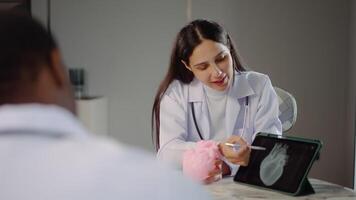 Due cardiologi impegnare nel un' dettagliato discussione su cuore malattia trattamento, utilizzando un anatomico modello per illustrare loro punti mentre consulenza con un' medico stagista nel un' clinica, Condividere conoscenza video