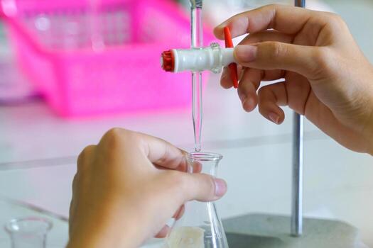 Close-up of hands meticulously operating a burette, dripping liquid into a lab flask. Emphasizes precision and detail in a chemical experiment, with a softly blurred background. photo