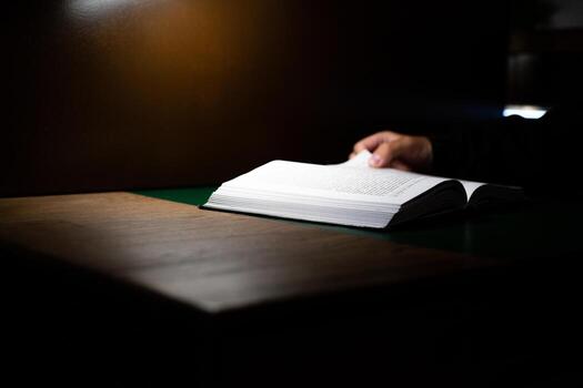 Person holding open book in dimly lit environment, perfect for emphasizing the power of reading and learning in solitude. The image reflects focus, reflection, and intellectual engagement photo