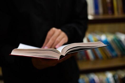Person standing in library holding open book, surrounded by rows of books. Tactile experience of reading and quiet, contemplative nature of libraries. The moment conveys curiosity photo