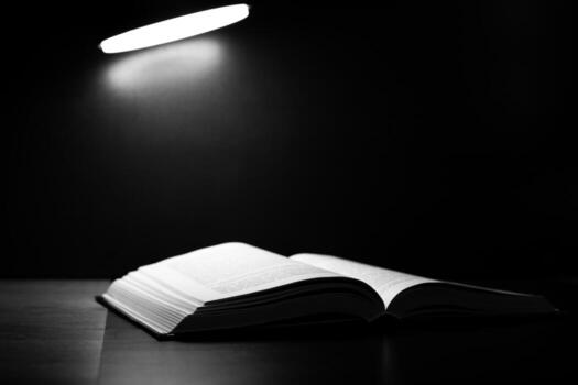 Close up of open book under single light source. Dramatic shadows and contrast create feeling of solitude and concentration, perfect for intimate reading experience or deep reflection photo