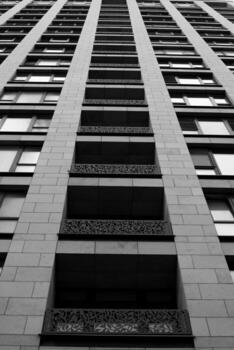 Black and white view of modern skyscraper with decorative balcony railings, architectural details, geometric patterns, and glass windows, shot from the ground up photo