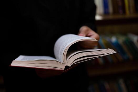 Person actively flipping through pages of book, focusing on searching for information for study or academic work, set against backdrop of library environment filled with educational resources photo