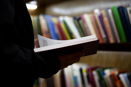 Hand holds an open book in midst of vast library, showcasing crisp pages of hardcover. Essence of peaceful reading and learning, moment of discovery in world of knowledge photo
