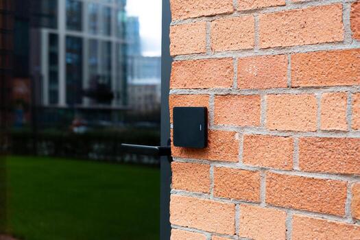 Modern access control system with RFID card reader attached to brick wall. Photo highlights blend of traditional architecture with contemporary security technology in urban setting