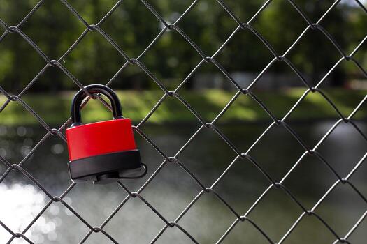 Padlock on a fence, symbolizing control, boundaries, and the restriction of access. The serene natural background contrasts with the idea of confinement and security photo