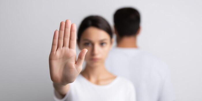 Young woman with a raised hand signaling stop, standing in front of a man with a neutral expression, conveying a message of boundaries and personal space in a minimalistic setting photo