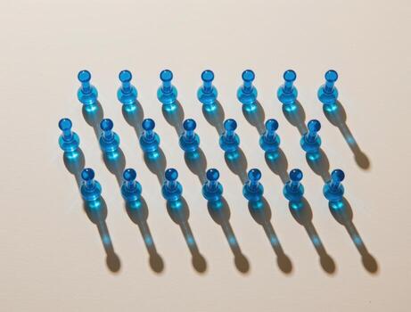 Blue push pins forming a grid with long shadows on white background photo