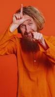 Caucasian man showing loser gesture and pointing on you, blaming accusing for unsuccess, expressing disrespect, mocking your failure, bullying abuse. Young guy isolated on orange background indoors video
