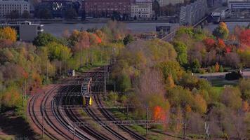 aereo Visualizza Spettacoli un' giallo pendolare treno curvatura per il ferrovia ponte nel riga, autunno alberi e sul fiume edifici visibile, morbido leggero Aggiunge struttura e profondità. video