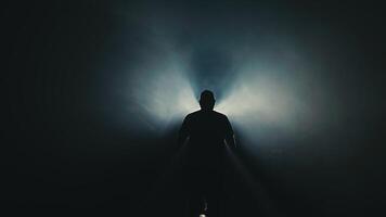 silhuett av en man framväxande från skuggor, upplyst förbi en mjuk ljus källa, skapande en dramatisk atmosfär av mysterium och förväntan i en mörkare miljö video