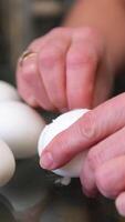 Overhead view of fair skinned person focused on peeling shell off boiled egg over bowl on table with scattered shell fragments, on placemat beside potatoes and empty dish video