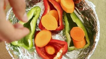 Hand drops sliced carrot over colorful pepper base, each carrot piece adding texture and depth. Bright carrot contrast with smooth pepper halves. Concept of carrot layering in vegetable preparation. video