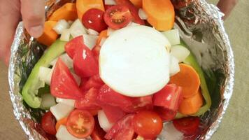 Hand places halved onion atop layered vegetables, onion adding bold texture and tone. Surrounded by foil and color, onion becomes final accent in prep. Concept of onion in food composition. video