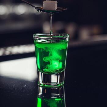 A sugar cube is slowly dissolved into a vibrant green absinthe cocktail in a shot glass creating a mesmerizing cloudy effect photo