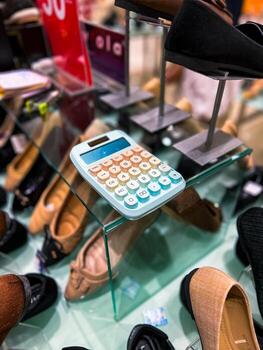 A calculator can be found resting on top of a sleek glass shelf, which is thoughtfully arranged and surrounded by various shoes in a retail display photo