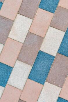 Interlocking textured paver blocks creating a seamless diagonal pattern, showcasing a surface comprising a variety of shades of blue, brown, beige, and peach colored pavement photo