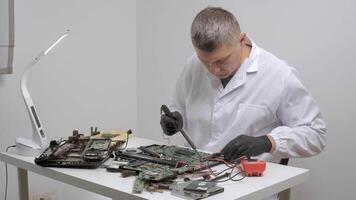 Engineer repairing electronic circuit board using soldering tool at desk, Technician in white coat working with motherboard and wires during precise electronics maintenance video
