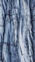 The aerial view reveals intricate patterns of deep crevasses and textured ice on a glacier in Iceland. Vertical shots video