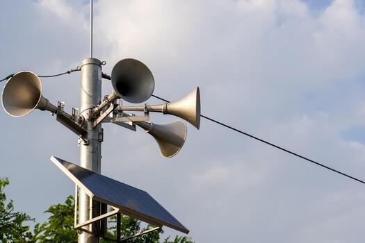 Solar-powered public address system with multiple loudspeakers mounted on a pole against a clear blue sky, signifying outdoor communication technology and emergency broadcasting capabilities photo