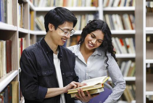 Student Exchange Program Concept. Two happy multiethnic students standing in university library, reading book, copyspace photo