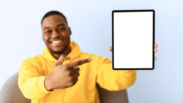 Check This Out. Happy Black Man Showing Digital Tablet Blank Screen Recommending Application Or Website Pointing Finger At Computer Over Gray Studio Background. Selective Focus, Mockup, Panorama photo