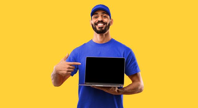 Arab Delivery Guy Showing Laptop Empty Screen Advertising Courier Service Or Website Smiling To Camera Standing In Studio Over Yellow Background. Man In Red Uniform Posing With Computer. Mockup photo