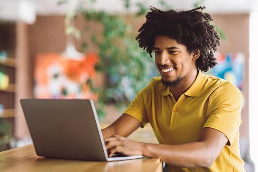 Online Communication. Black Happy Man Typing On Laptop While Sitting At Table In Cafe, Young African American Guy Using Computer While Relaxing In Cozy Cafeteria, Closeup Shot With Free Space photo