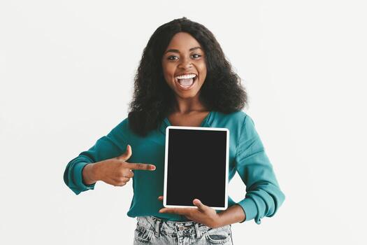 Emotional young black woman pointing at digital tablet with empty screen, modern pad with blank display, mockup, white studio background, various mobile applications for tablets concept photo