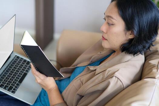 Close up view of a hand holding a notebook to view information while working on a laptop. Working from home, workspace. photo