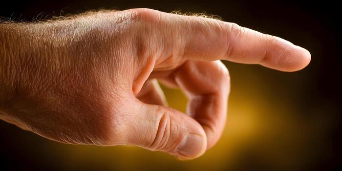 A hand with an index finger extended pointing forward against a dark and warm background photo