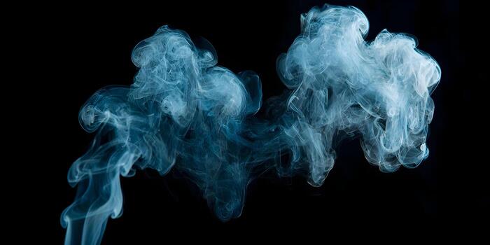 Wispy blue smoke patterns gently swirl and rise against a dark black background creating an ethereal abstract art effect photo