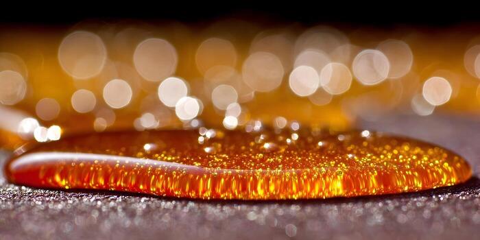 A shimmering golden liquid with tiny bubbles rests on a dark textured surface illuminated by bright bokeh lights photo