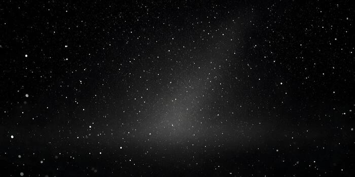 White particles resembling falling snow or stars float against a dark black background creating an abstract texture photo