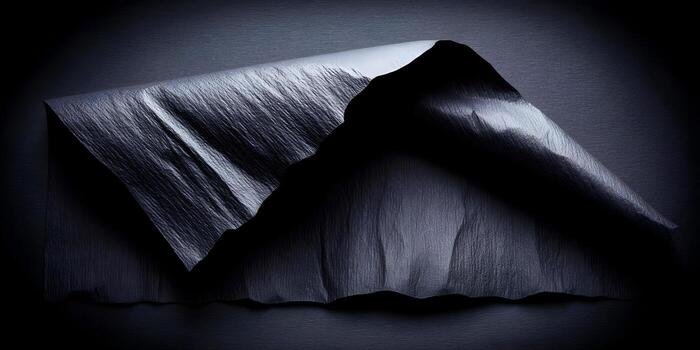 Dark textured paper is folded and draped creating abstract shapes and shadows photo