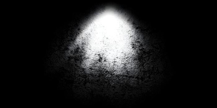 A bright spotlight illuminates a dark textured grunge wall creating a dramatic abstract background photo