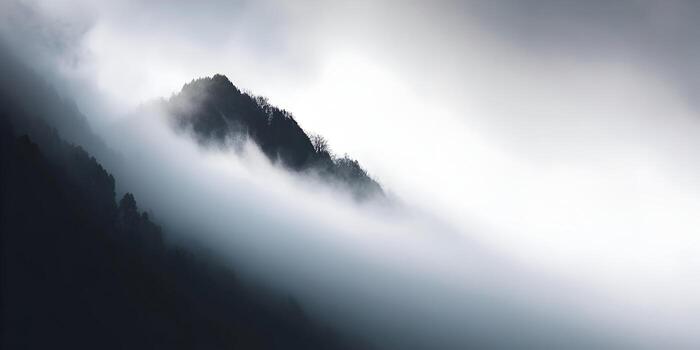 A majestic mountain range is enveloped in a thick layer of ethereal mist and fog creating a dramatic and moody natural landscape photo