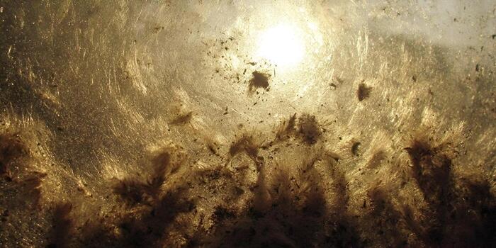 A bright sun shines through a heavily soiled and dusty glass surface creating an abstract texture photo