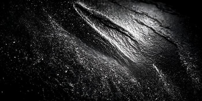 Dark rough rock surface features scattered white dust particles creating an abstract texture photo