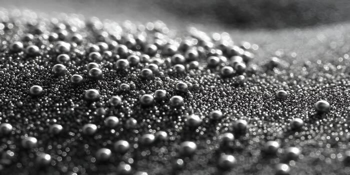 Shiny metallic spheres of various sizes are scattered on a granular dark surface creating a detailed texture photo