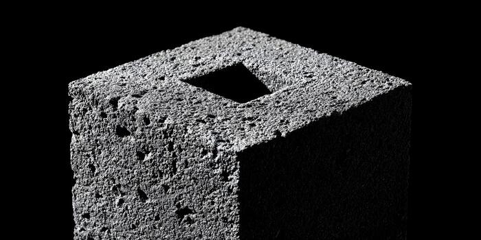 A detailed close up of a textured dark gray block featuring a precise square hole on its surface against a black backdrop photo
