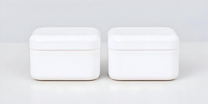 Two identical white square containers with rounded corners are displayed on a light gray surface against a plain background photo
