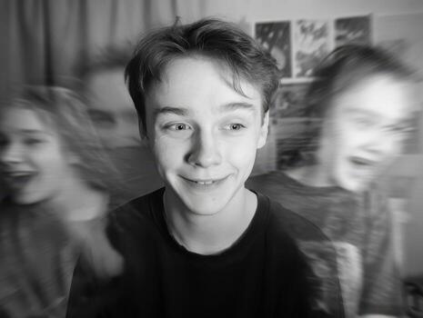 Smiling young person in center with blurred laughing figures on sides, creating a dynamic, playful effect. Black and white portrait, background includes various indistinct images photo