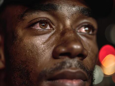 Close-up of a man's face with visible emotions, rough skin texture, and focused gaze. Eyes are highlighted against blurred lights in the background, suggesting night or urban setting photo