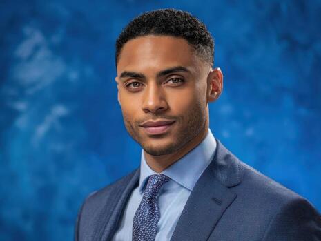 Professional man in a tailored suit, gazing confidently with a slight smile. Dark curly hair and well-groomed facial features create a sophisticated appearance. Blue patterned tie complements attire photo