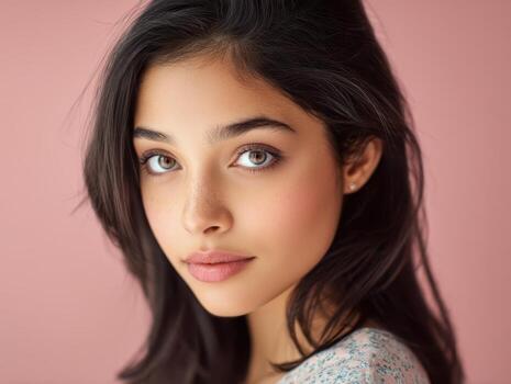 Young woman with long dark hair and expressive eyes looks gently towards the camera. Her subtle makeup and calm expression create a serene atmosphere, while wearing a soft-patterned top photo