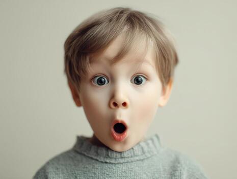 Young child with wide eyes and open mouth, wearing a gray knitted sweater. The expression suggests surprise. The light-haired child is against a plain background, emphasizing the emotion photo