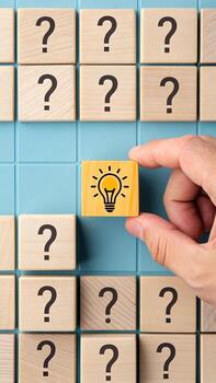 Hand selecting light bulb idea block from question marks photo