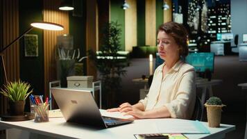 dipendente lavori dopo ore organizzazione e programmazione compiti per un' aziendale progetto. circondato di File, lei si concentra su budgeting e obiettivi per raggiungere azienda obiettivi a notte. telecamera un. video